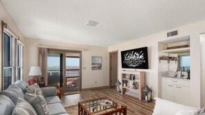 A living room with a sofa, a coffee bar, and a TV displaying 'Coastal Carolina Vacations and Sales'.