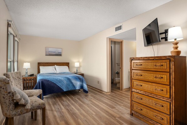 A hotel room with a bed, a chair, a dresser, a television, and a window.