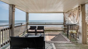 A covered outdoor area with a view of the beach, featuring wicker furniture and a table.