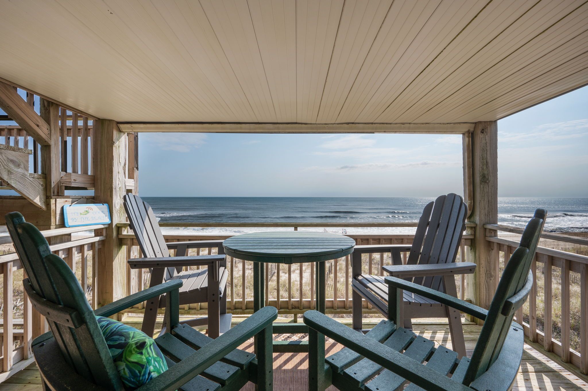 A wooden deck with Adirondack chairs and a table overlooking the ocean.