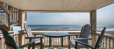 A wooden deck with Adirondack chairs and a table overlooking the ocean.
