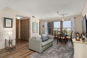 A living room with a checkered sofa, a dining table with chairs, a lamp, and a framed map on the wall. - Carolina Ocean Views: Dog Friendly, Ocean Views (Kill Devil Hills)