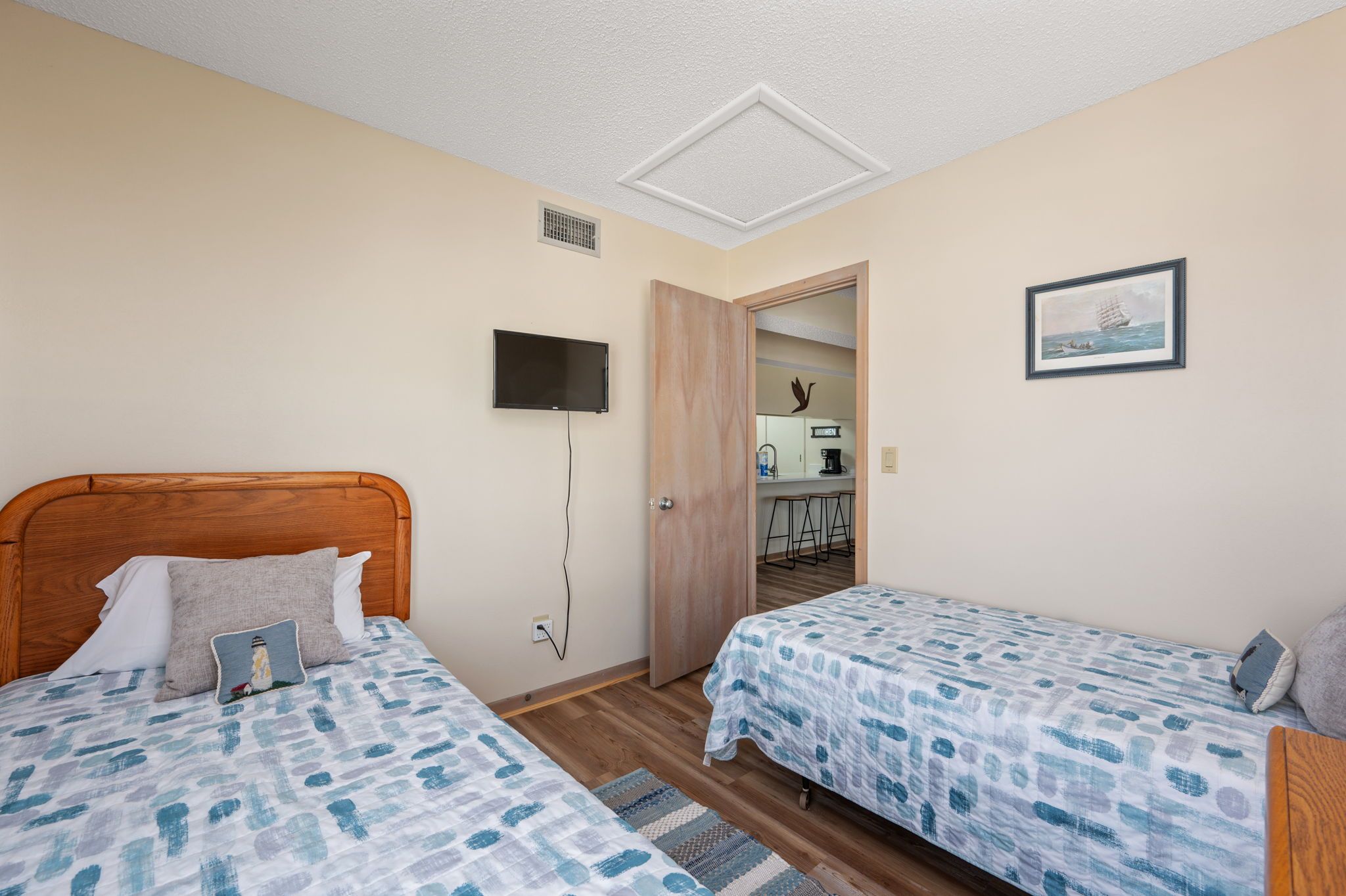 Ein Hotelzimmer mit zwei Betten, einem Fernseher, einem Gemälde und einer kleinen Küche im Hintergrund.