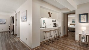 A modern hotel room with a wooden floor, a kitchenette, a dining area with stools, and a bed with a view. - Carolina Ocean Views: Dog Friendly, Ocean Views (Kill Devil Hills)