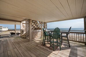 A wooden deck with a table and chairs, overlooking a beach.