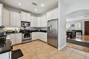 A modern kitchen with white cabinets, stainless steel appliances, and a pool table in the adjacent room. - Game Room House, Sleeps 12, Near Everything Tampa (Tampa)