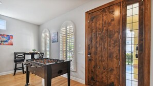A room with a foosball table, a wooden door, and a window with shutters.