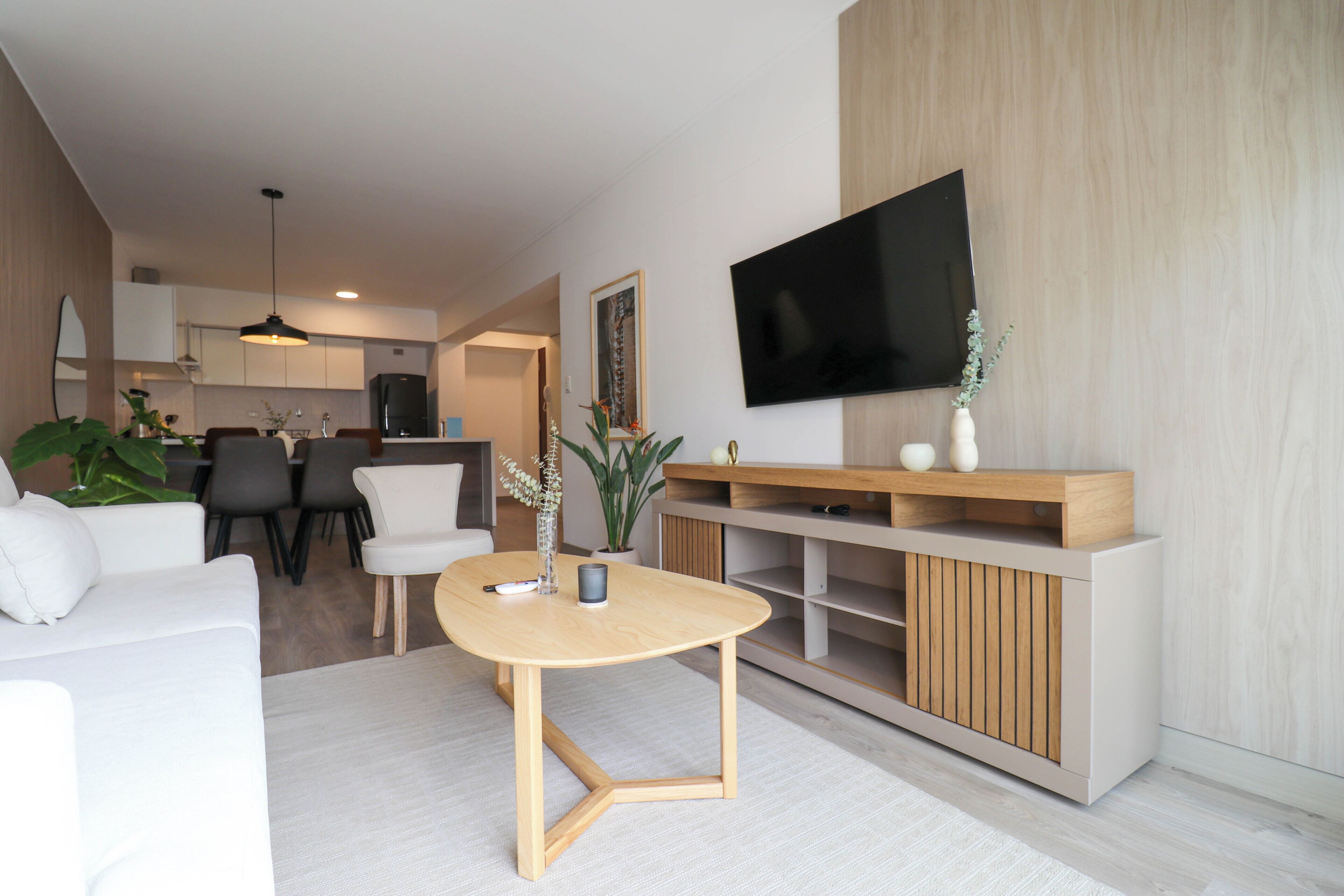 A modern living room with a wooden coffee table, white sofa, and a TV mounted on the wall.