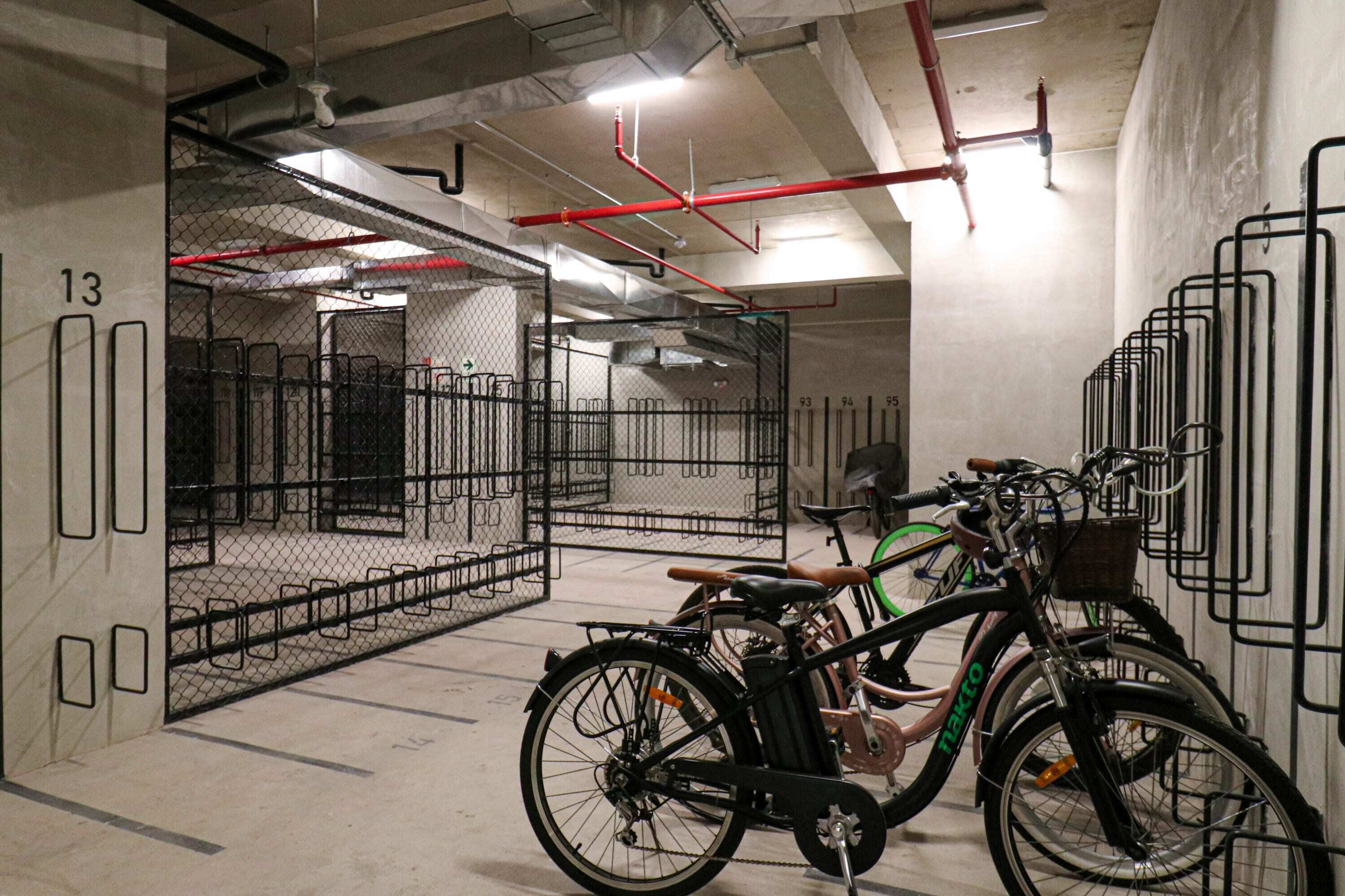 Een fietsenrek met meerdere fietsen, een hek van gaas en een betonnen vloer.