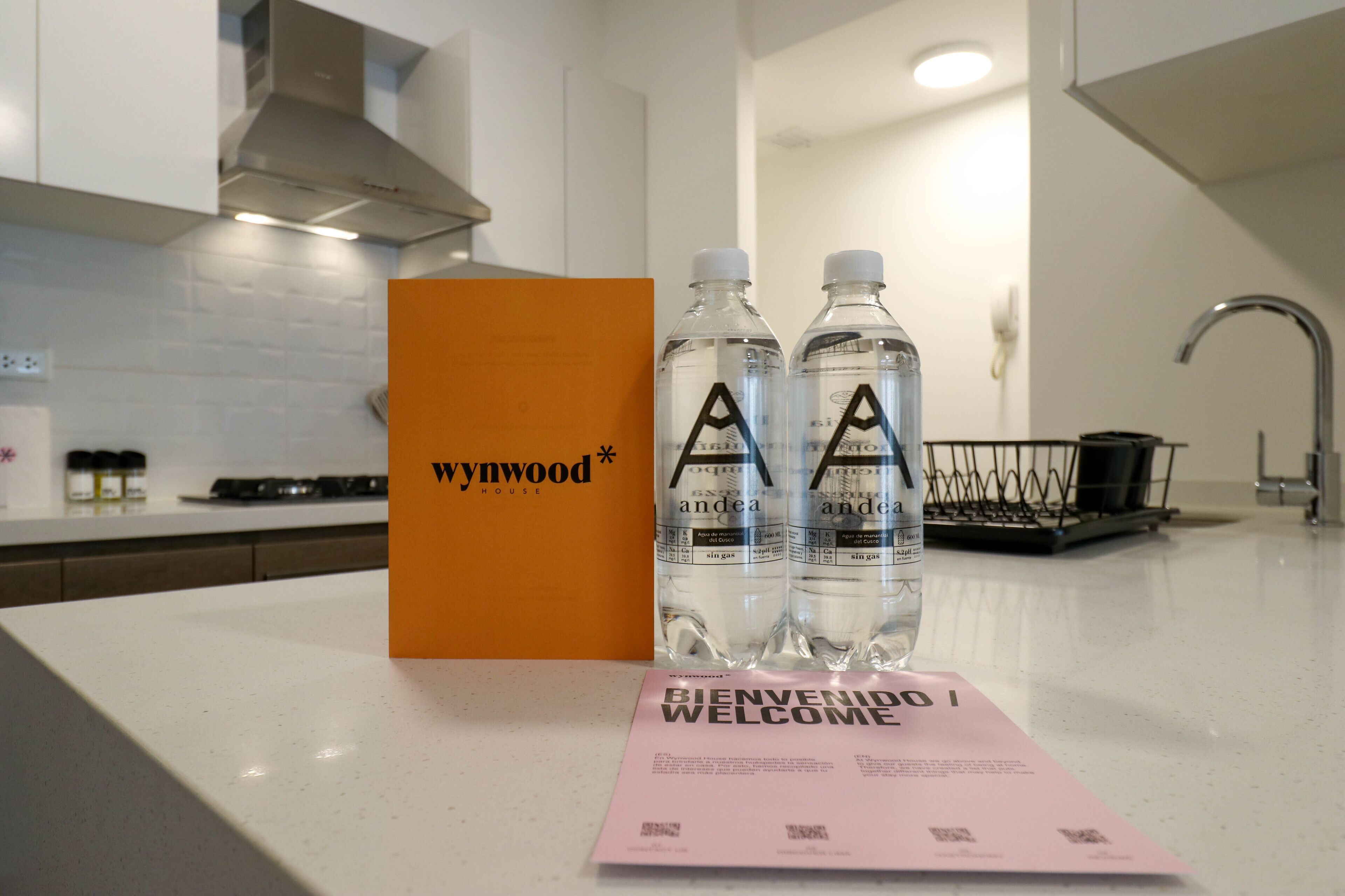 Una encimera de cocina con una tarjeta de bienvenida, dos botellas de agua y una caja naranja con el logo de la marca.