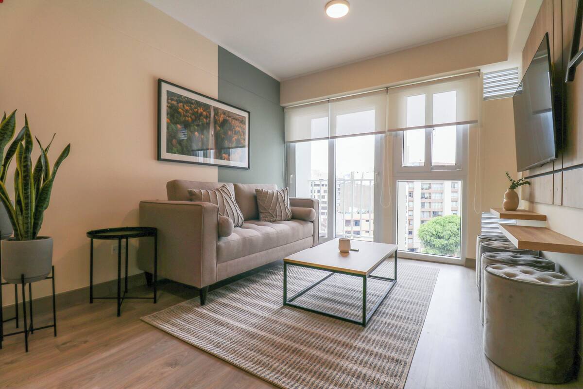 A modern living room with a sofa, coffee table, and a large window with a view of buildings.