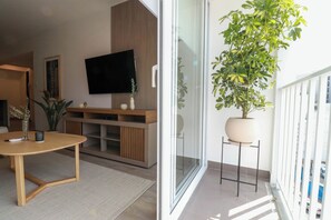 A modern living room with a flat-screen TV, wooden furniture, a glass door leading to a balcony with a potted plant. - Wynwood Kennedy in Miraflores (Lima)