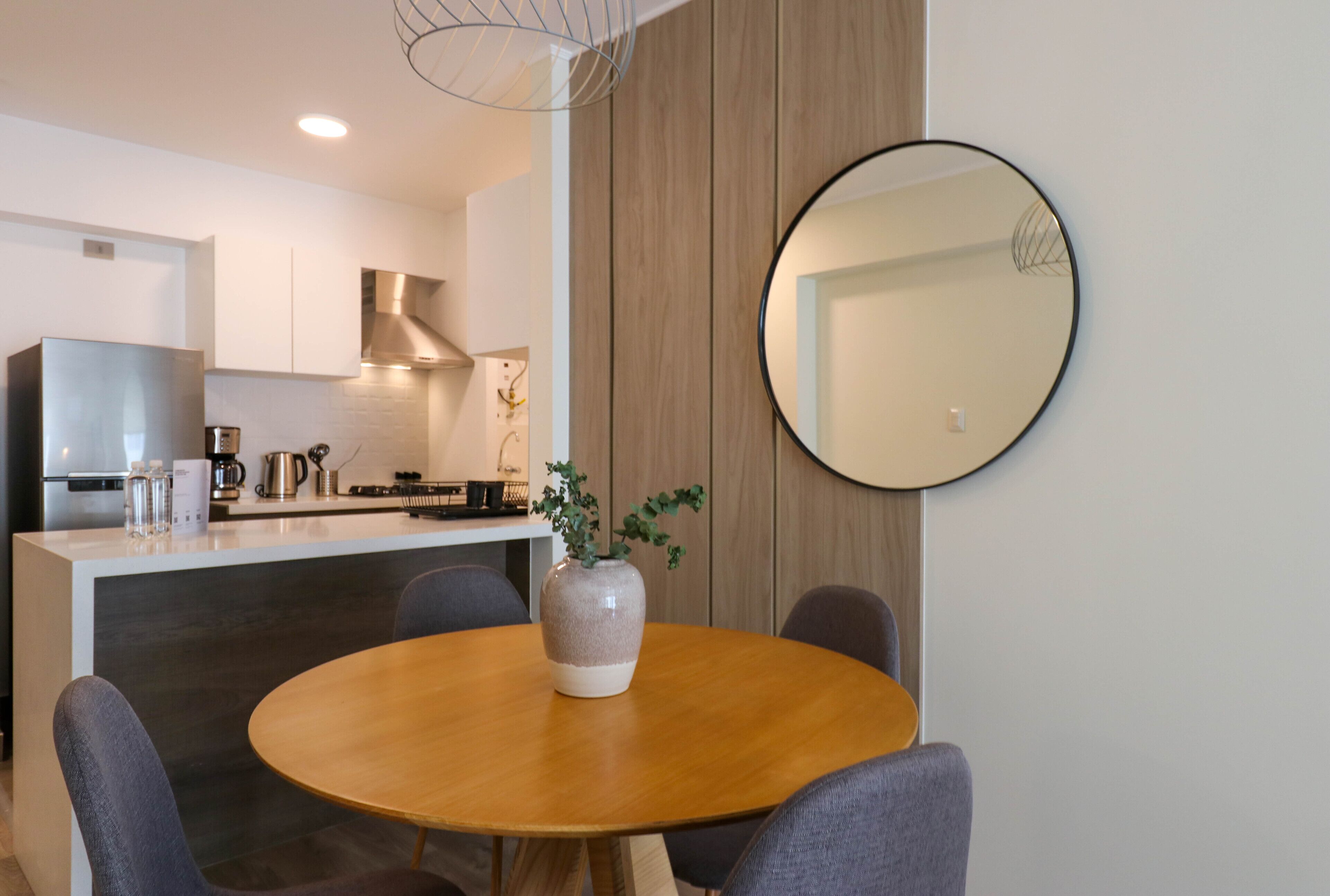 Una cocina moderna con una isla central, un comedor con mesa redonda y un espejo grande en la pared.