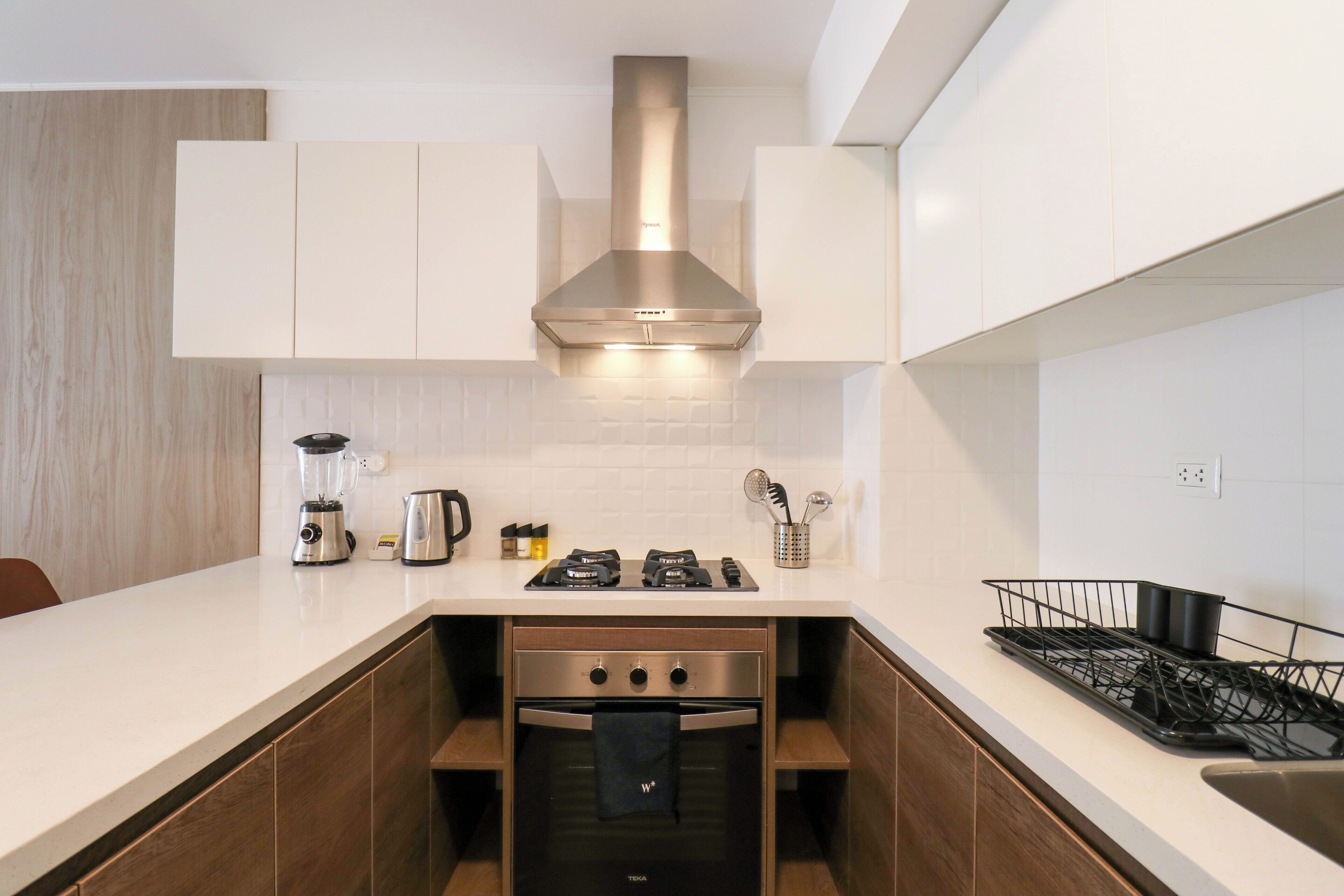 A modern kitchen with a built-in oven, a stove, and a stainless steel range hood.