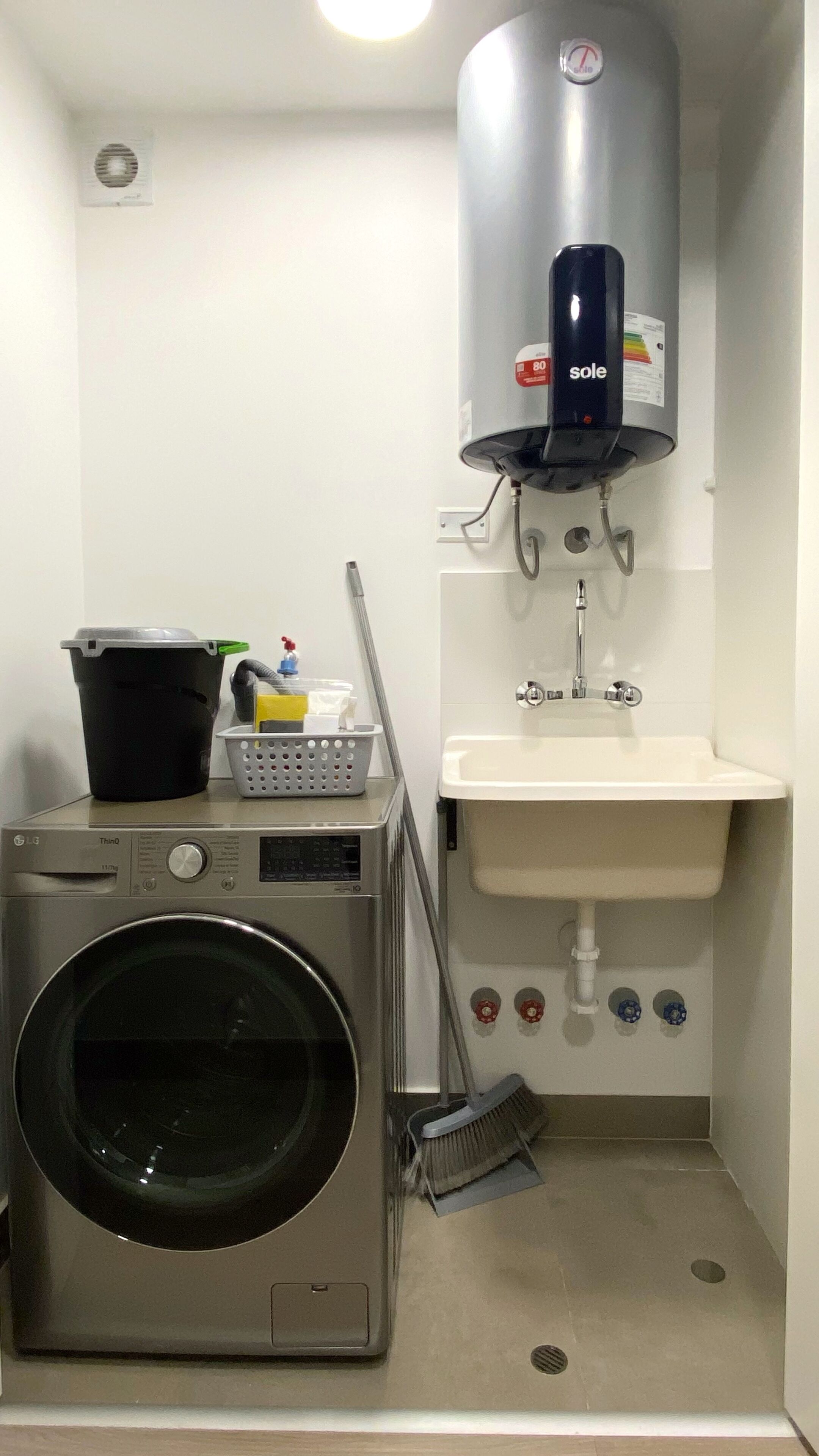 A compact laundry room with a washing machine, a sink, and a heater.