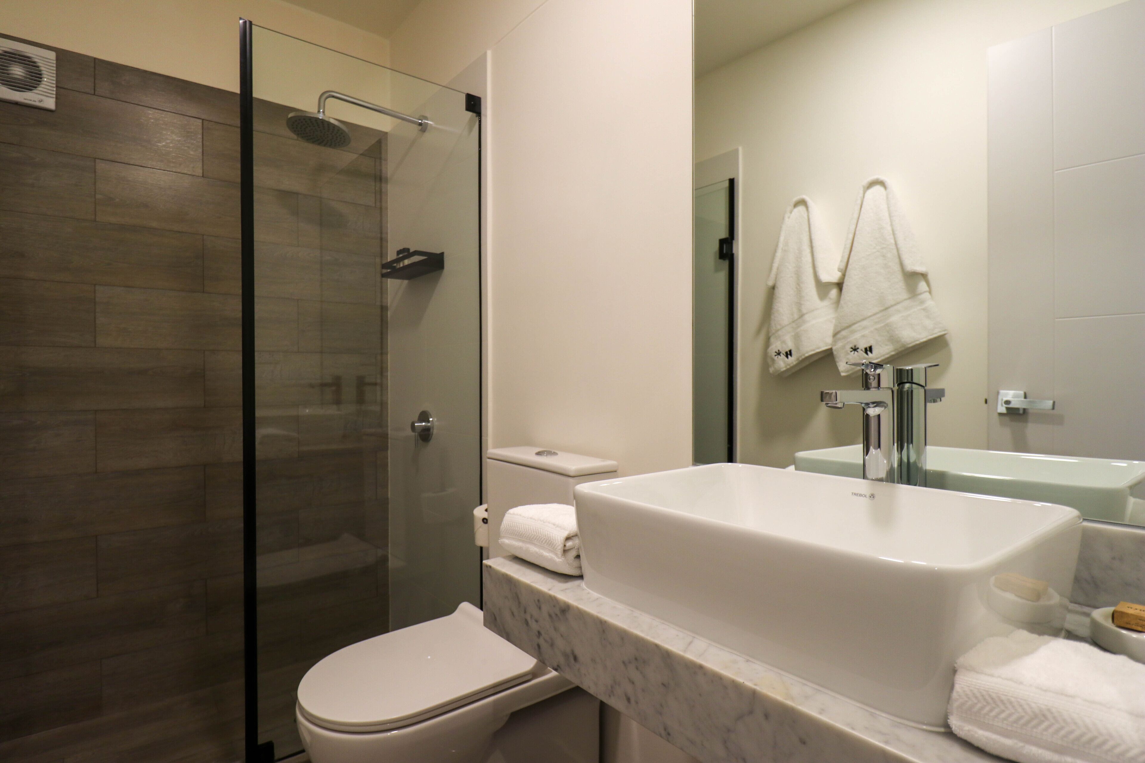 Een moderne badkamer met een douchecabine van glas, een wit toilet, een groot wit wastafel en twee handdoeken aan de muur.