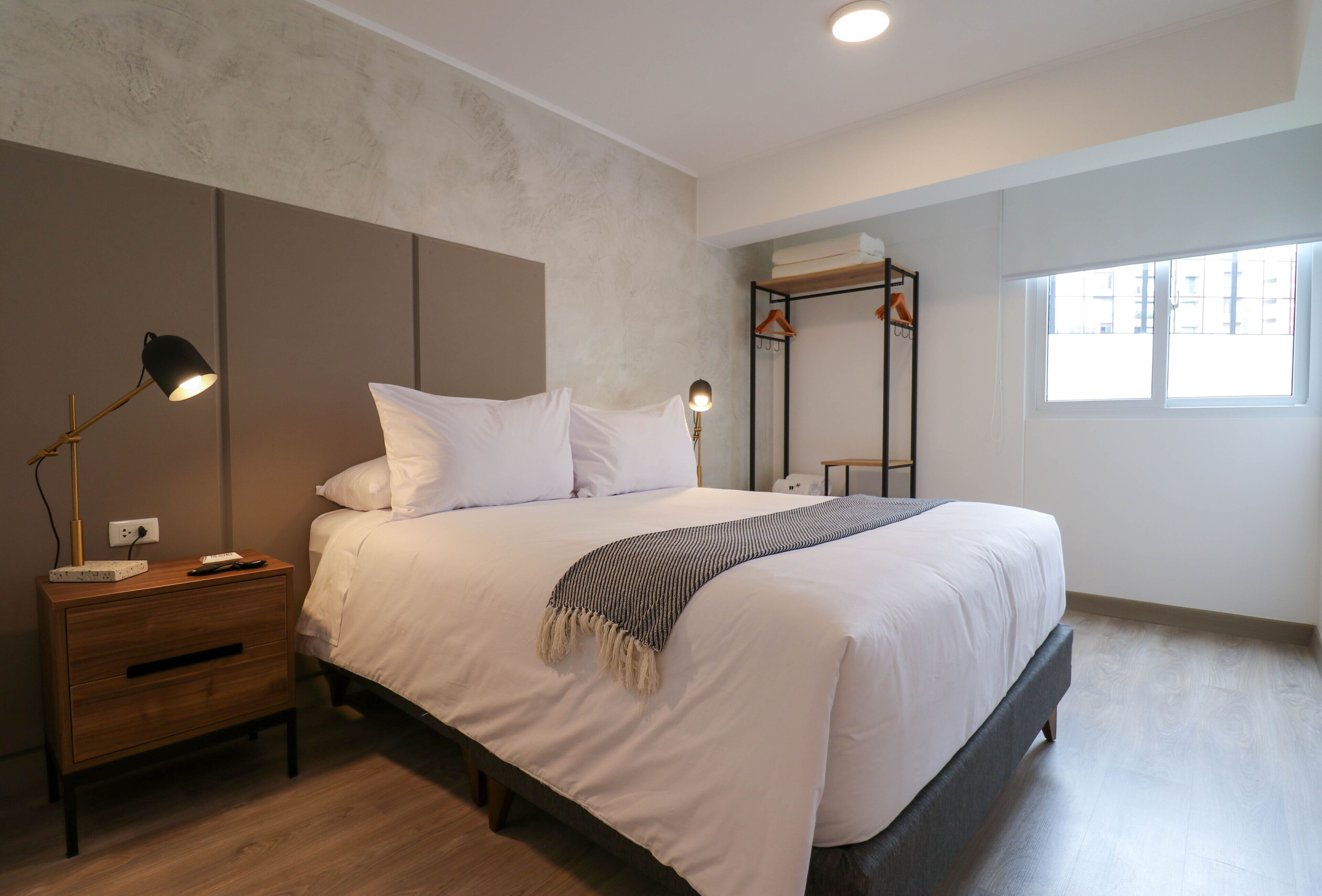 Un dormitorio moderno con una cama grande, mesitas de noche, un armario y una ventana.