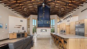 A spacious kitchen with a large island, wooden cabinets, and a high ceiling with exposed beams.