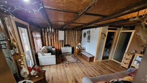 A cozy living room with wooden floors, a sofa, a white armchair, and a small table with a lamp. - Relaxing rustic cabin on the lake 25 feet from the shore. (Baileyville)