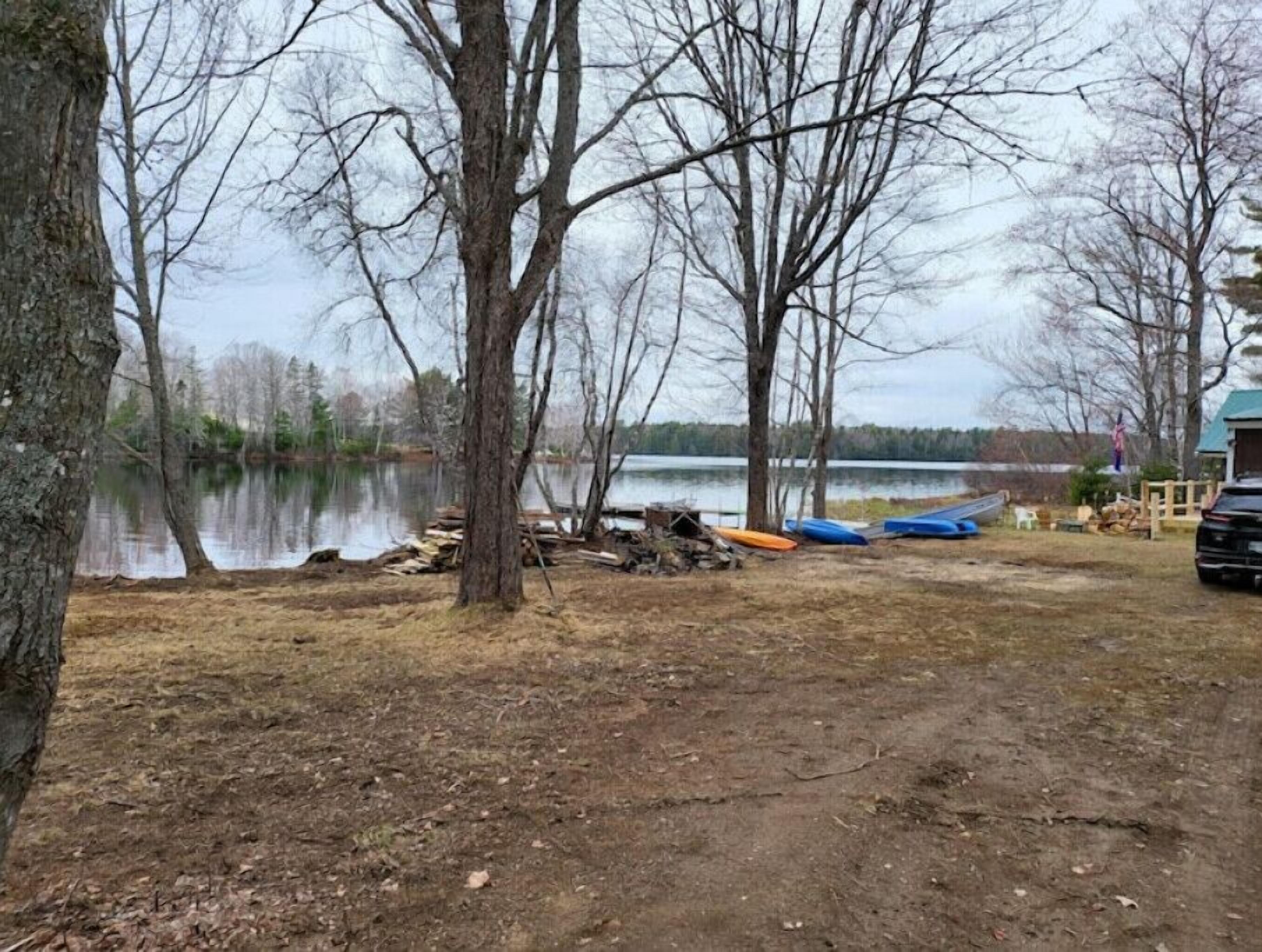 Ett område vid en sjö med träd, en brygga och en parkerad bil i närheten.