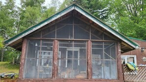 A rustic cabin with a large window, wooden lattice front, and a green roof. - Relaxing rustic cabin on the lake 25 feet from the shore. (Baileyville)