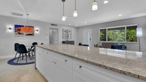 Una cocina moderna con armarios blancos, encimeras de granito, iluminación colgante y un comedor con mesa y sillas.