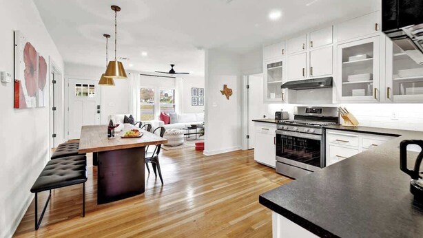 A modern kitchen with white cabinets, a central island, and a dining area with a bench.