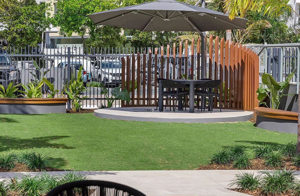 Un espace extérieur circulaire aménagé avec une table et des chaises, entouré d’une clôture en bois et surmonté d’un grand parasol.