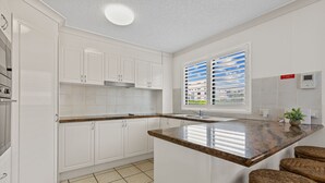 Una cocina moderna con armarios blancos, encimera de granito, estufa empotrada y una ventana con persianas.