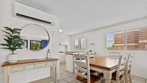 Un comedor con una mesa y sillas de madera, un armario blanco con espejo y una planta en maceta.