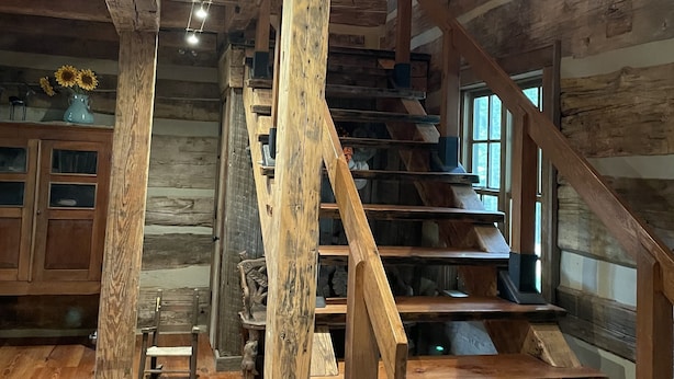 Una escalera de madera con un interior rústico, vigas de madera y un jarrón con girasoles.