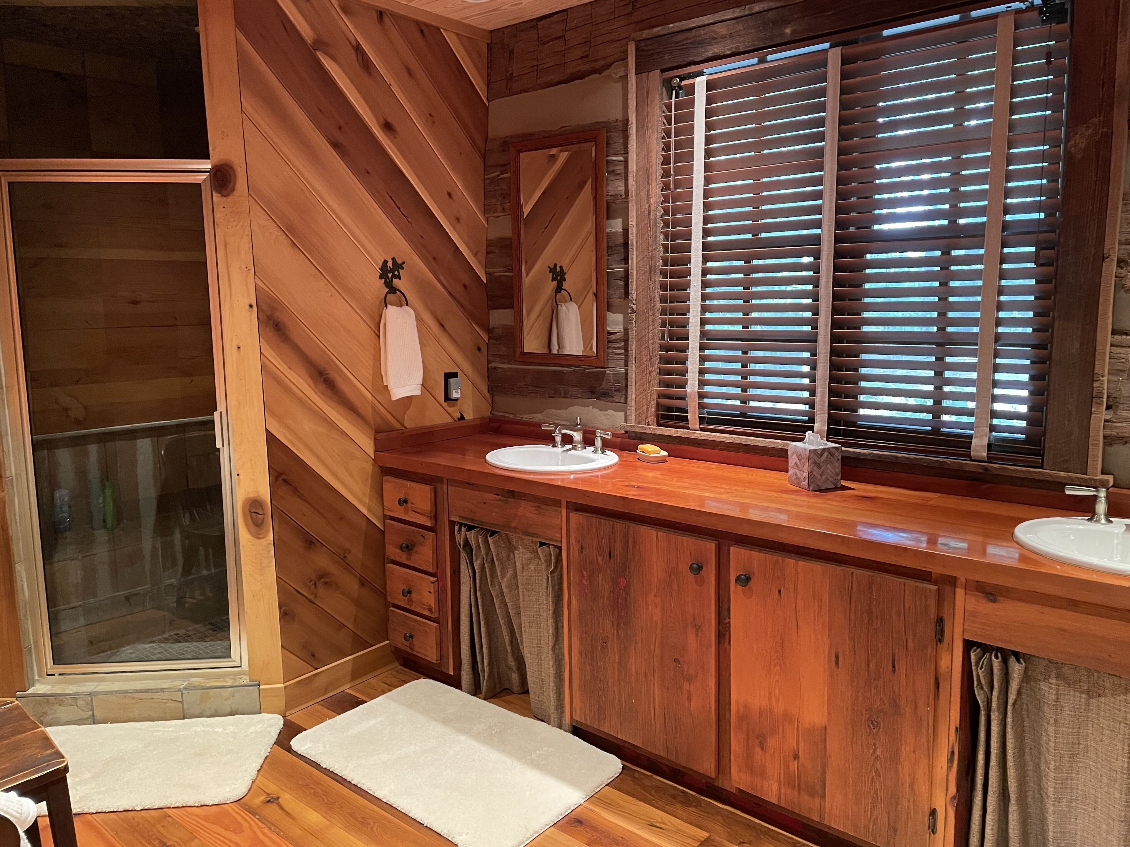 Baño de cabaña de madera con un ventanal grande, muebles de madera, un lavabo y una ducha.