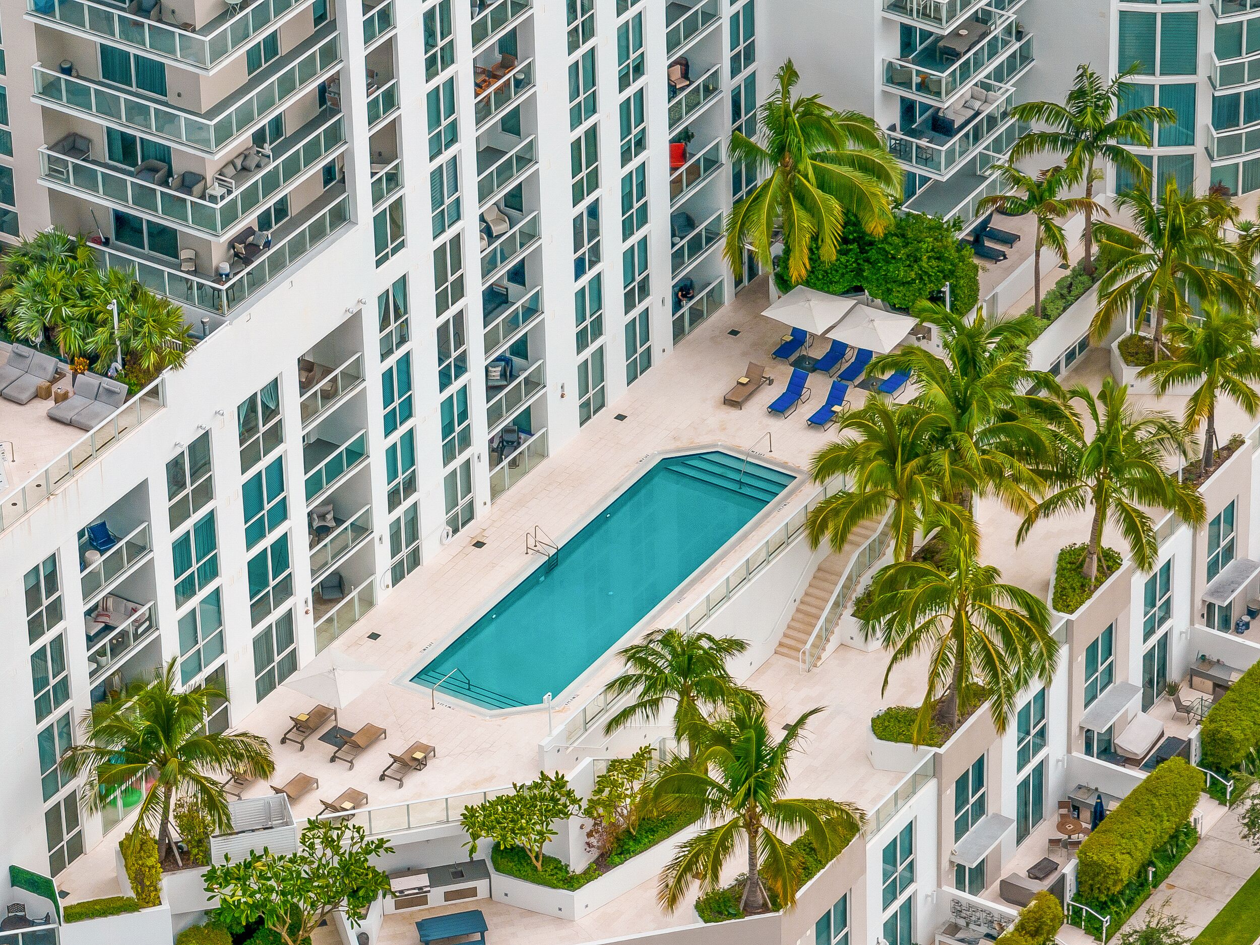 Hotel alto com piscina no terraço, rodeado por palmeiras e espreguiçadeiras.