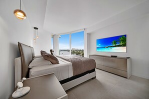 A modern bedroom with a large window, a bed, a TV, and a bedside table. - Ocean view Amazing 3BR at Tiffany House (Fort Lauderdale)