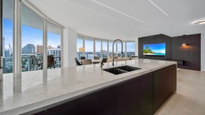 A modern kitchen with a large island, a built-in sink, and a flat-screen TV. - Ocean view Amazing 3BR at Tiffany House (Fort Lauderdale)