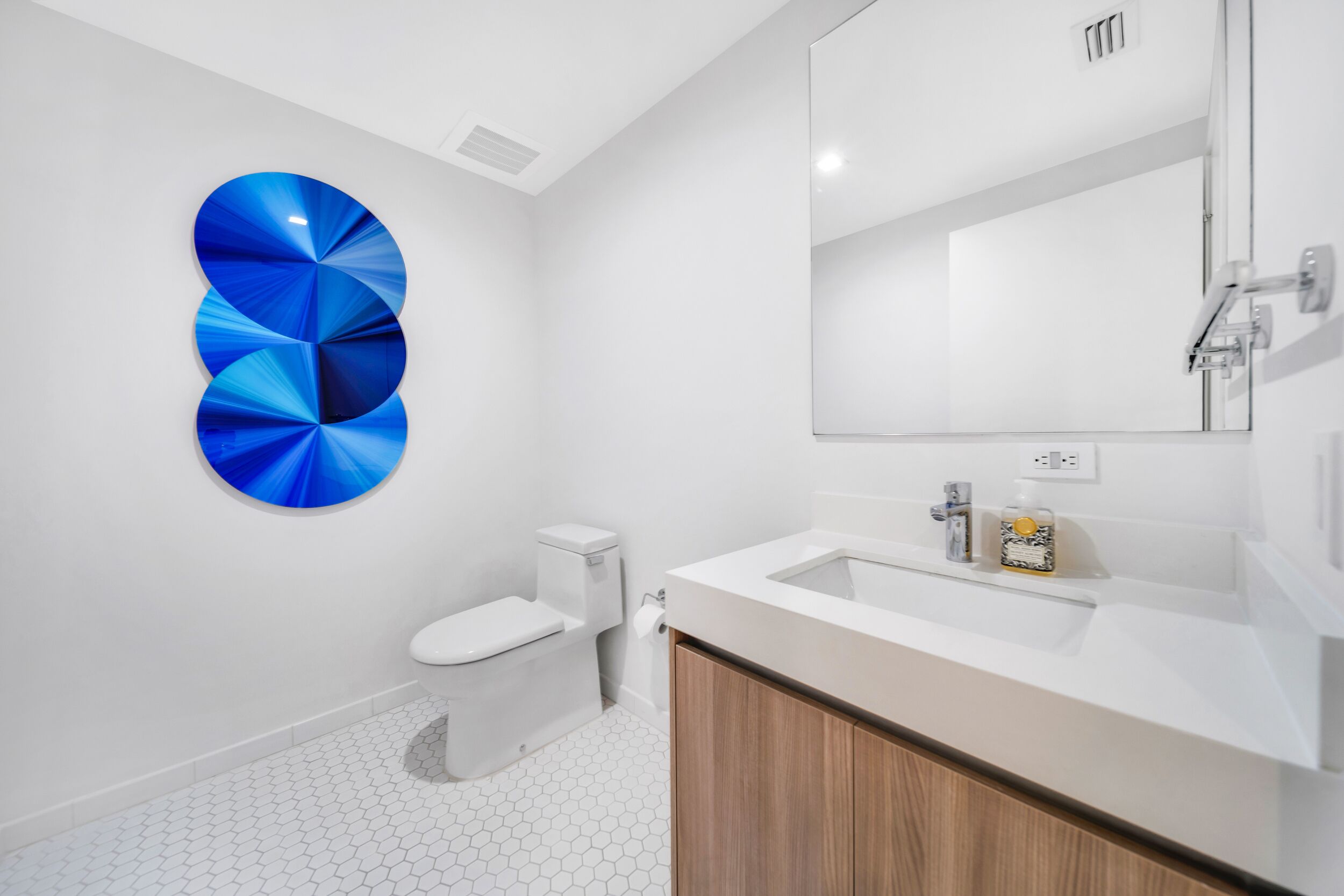 A modern bathroom with a white toilet, a wooden cabinet, a white sink, and a large mirror.