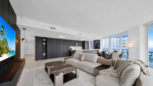 A modern living room with a large flat-screen TV, a sofa, a coffee table, and a dining area with a table and chairs. - Ocean view Amazing 3BR at Tiffany House (Fort Lauderdale)