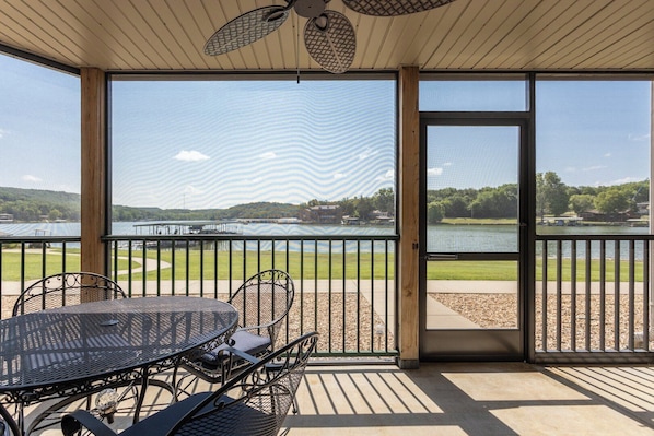 A covered outdoor area with a table and chairs, a view of a lake, and a dock in the background.