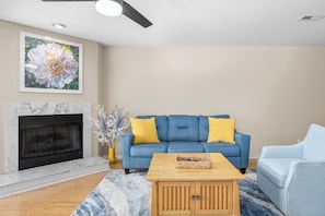 Ein Wohnzimmer mit Kamin, blauem Sofa, gelben Kissen, einem Couchtisch und einem Gemälde an der Wand.