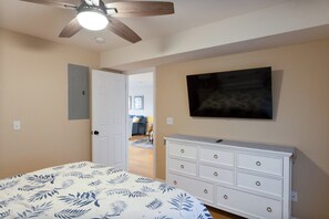 Ein Schlafzimmer mit Bett, Kommode, Deckenventilator und Fernseher.