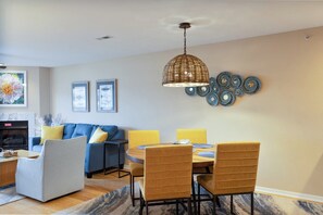 A dining area with a round table, four chairs, a hanging light fixture, and wall decor.