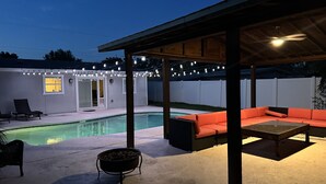 Un jardin avec une piscine, un espace salon extérieur et des guirlandes lumineuses.