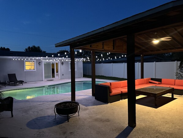 A backyard with a swimming pool, outdoor seating, and string lights.