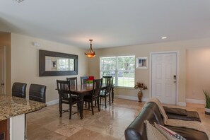 Un salon spacieux comprenant un coin repas, un grand miroir et une porte donnant sur l’extérieur.