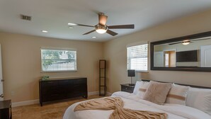 Une chambre à coucher comprenant un lit, un ventilateur de plafond, une commode, une table de chevet, un miroir et une fenêtre avec des stores.
