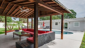 Un espace extérieur aménagé, abrité et doté d’une piscine, de poutres en bois et d’un canapé rouge.