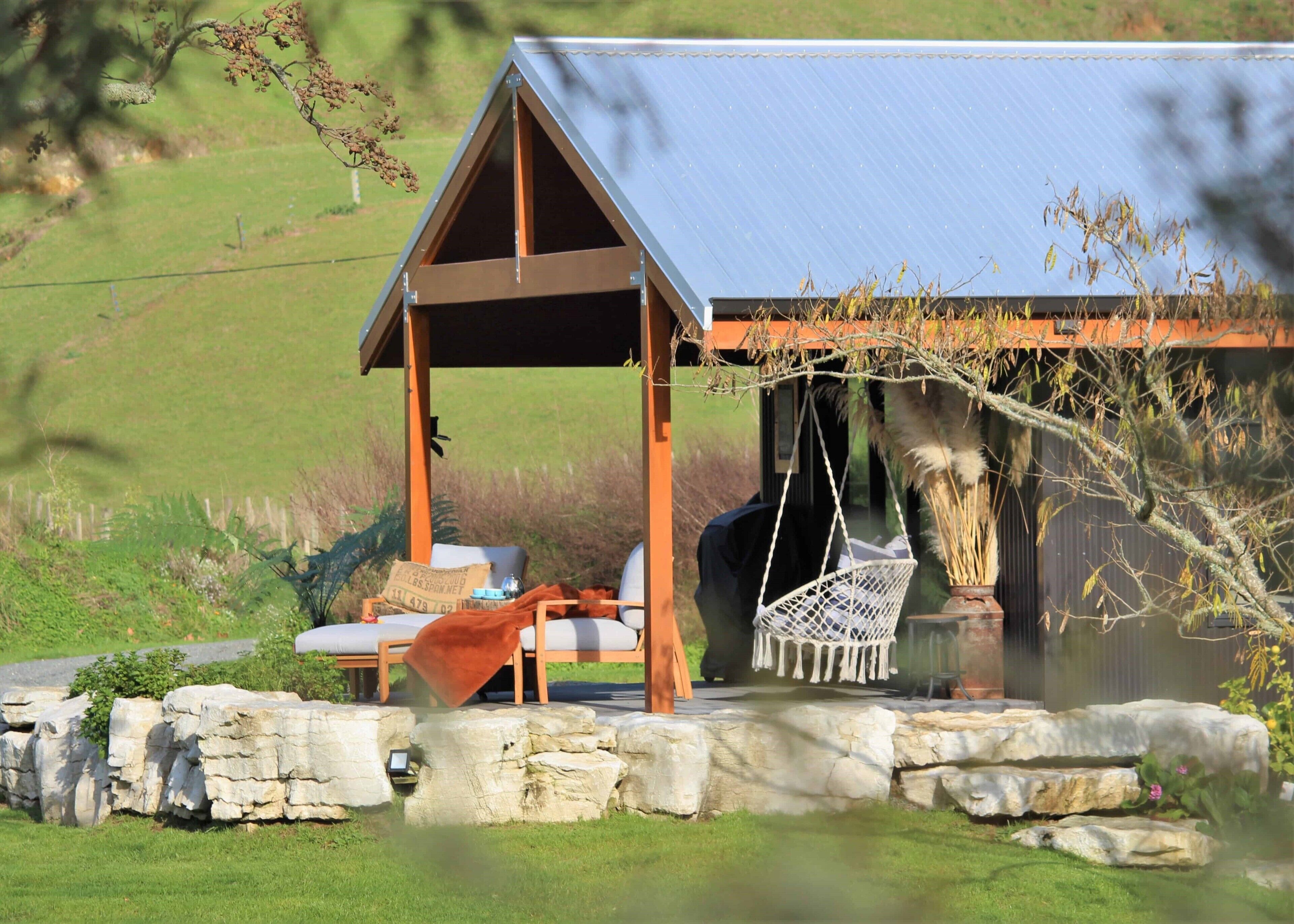A rustic outdoor seating area with a wooden pergola, stone walls, and a hanging chair.