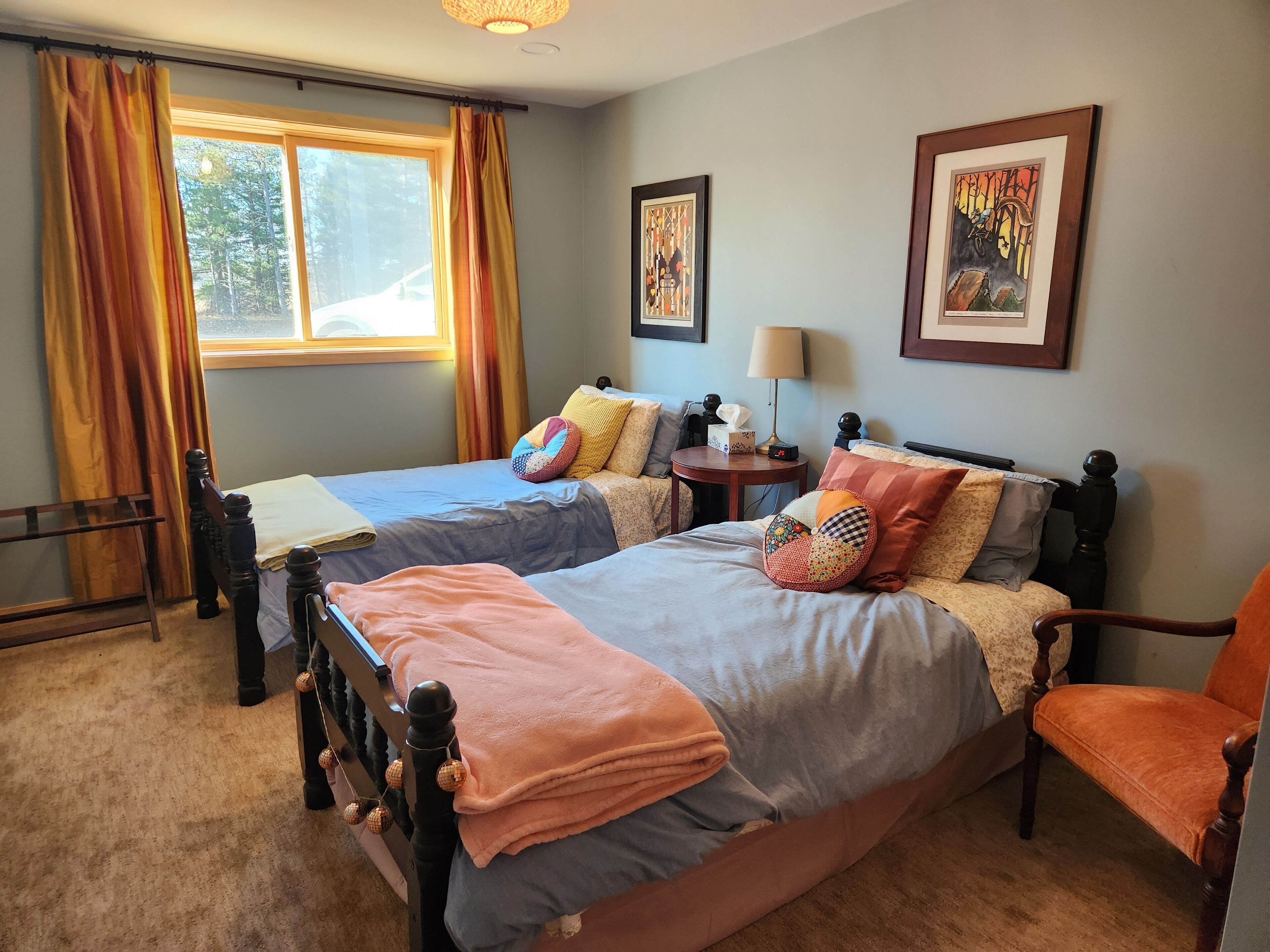 A bedroom with two beds, a chair, a nightstand, and a window with curtains.