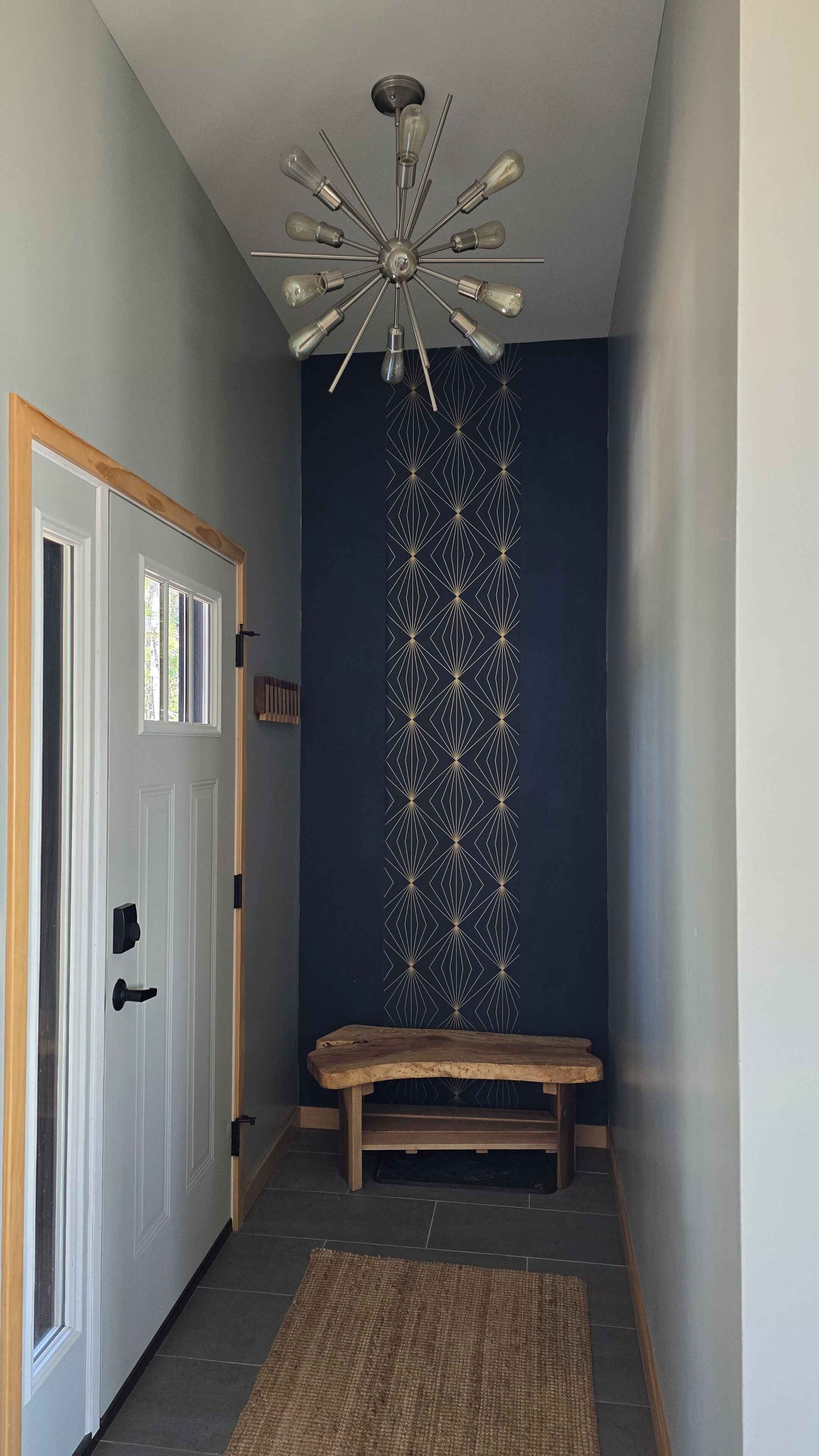 Un corridoio con una porta bianca, una panca, una parete decorata e un lampadario.