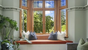 A bay window with a cushioned seat, a clear glass door, and a view of trees outside. - Heritage Apartment on City Fringe (Auckland)